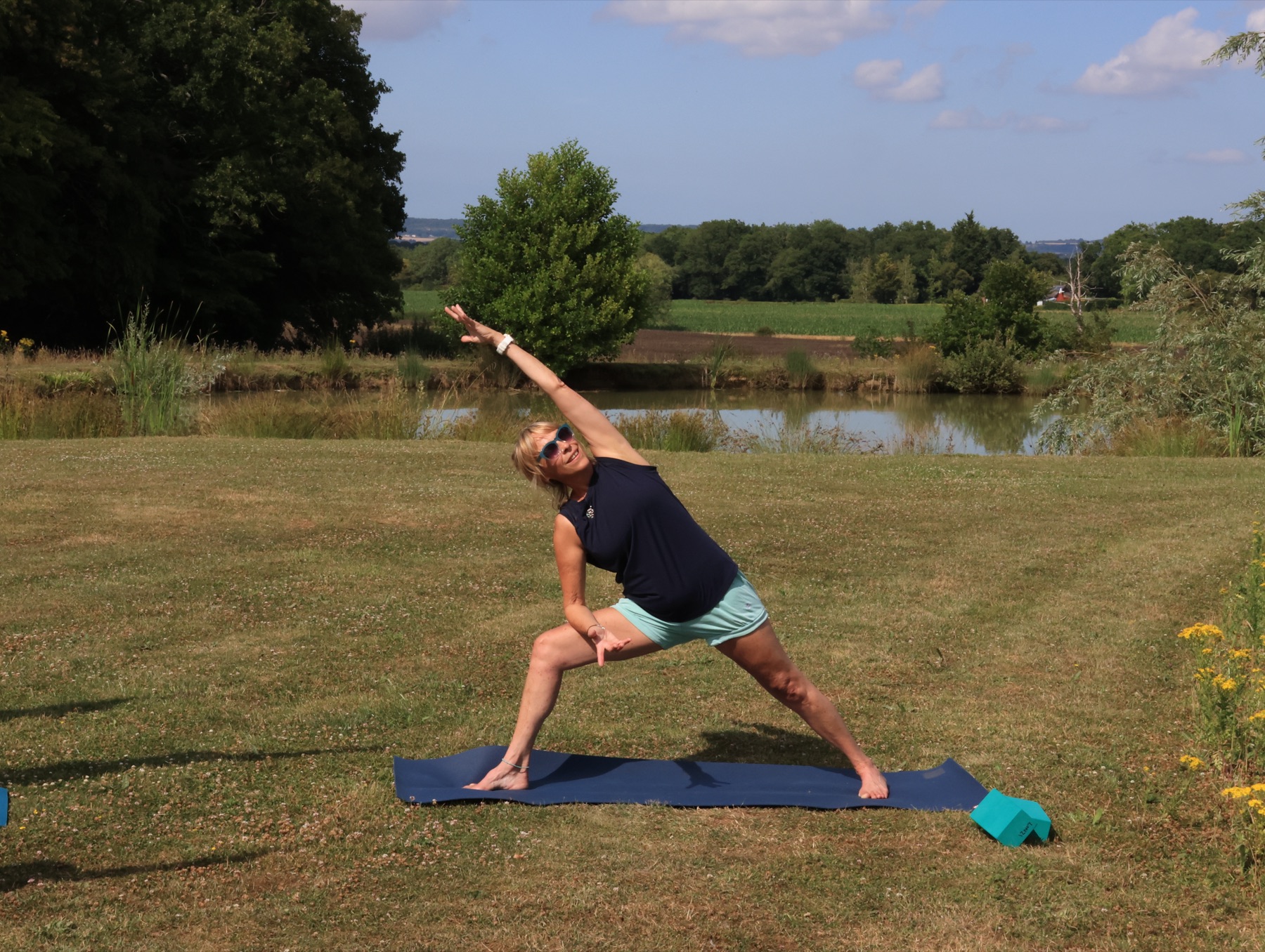 Linzi alone in extended side angle pose on her mat, with the lake and a dark treeline behind